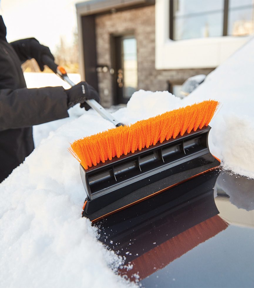 Balais à neige qui retire de la neige d'un capot de voiture noir